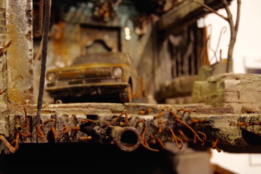 A detail of Um Shaham's miniature home, with exposed piping and wire filaments, and a singed car in the background. Lucy Gellman Photo.